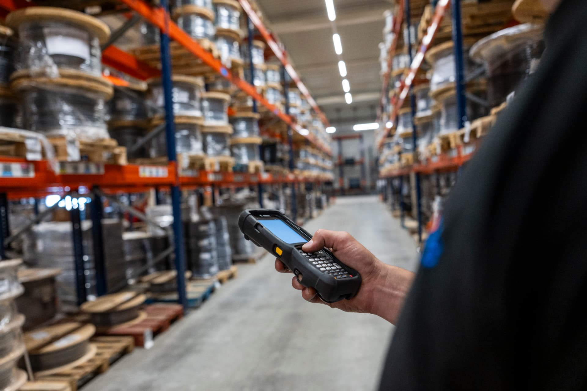 A warehouse colleague using a handheld scanner among shelves of cable reels